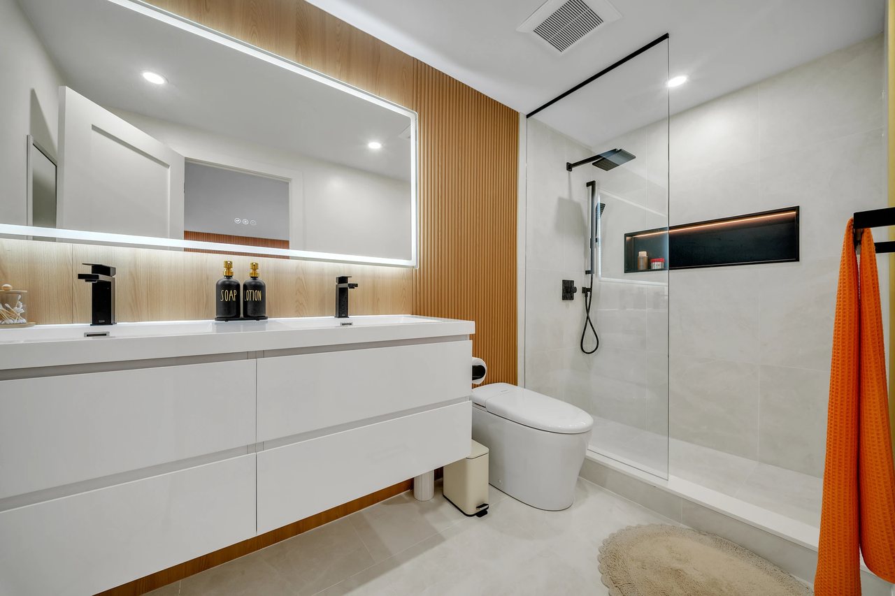 Bathroom with a white vanity, wide illuminated mirror, and glass shower.