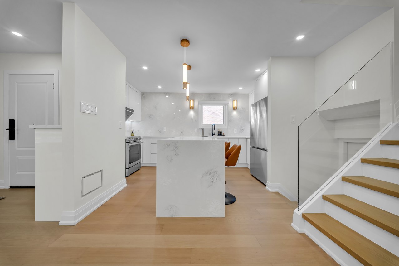 White kitchen island and pendant lights beside an open staircase with wood treads.