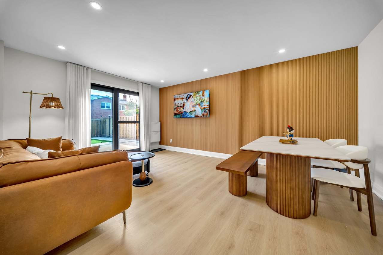 Open-plan dining and living space with a wood feature wall and glass doors.