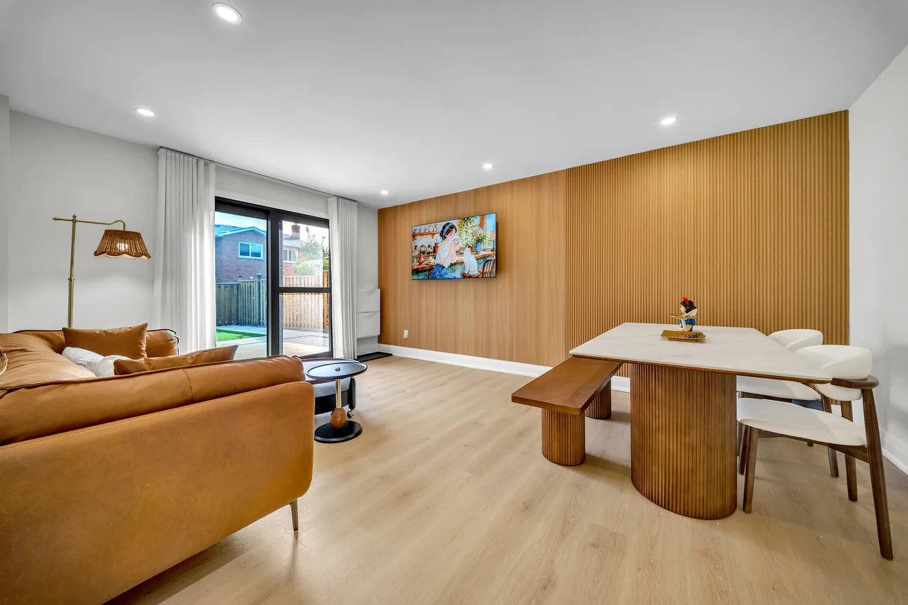 Open-plan dining and living space with a wood feature wall and glass doors.