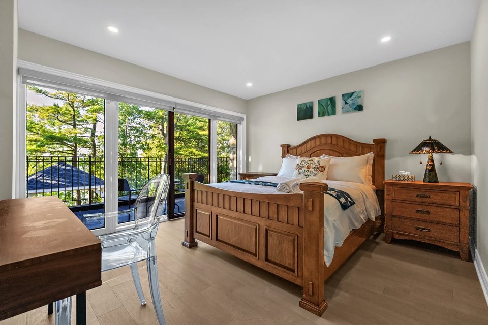 Real estate bedroom photography with natural light, a wood bed, and garden-facing windows.